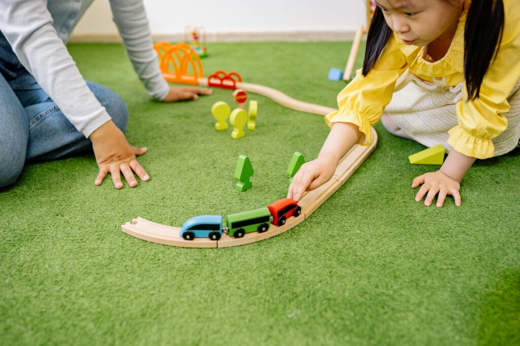 Young girl enjoying playtime with a wooden toy train indoors.